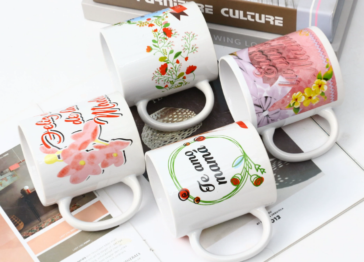 A collection of beautifully designed custom holiday mugs, each with a different festive design, sitting on a decorated office table.