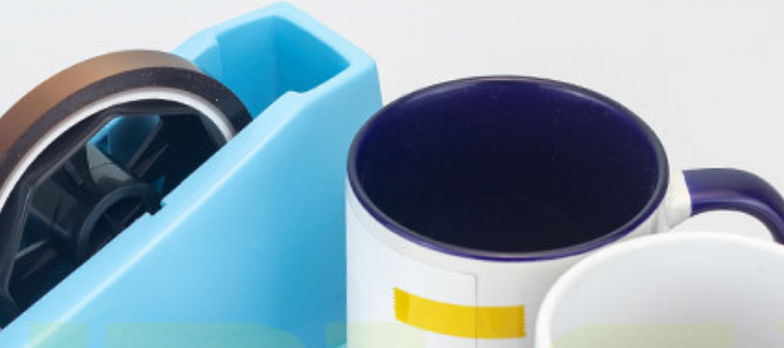 A close-up shot of a sublimation mug being prepared, with several pieces of yellow heat-resistant tape firmly securing the paper's seam, top, and bottom.